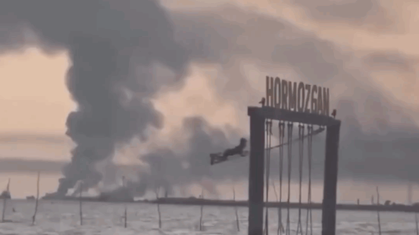 Menina brinca em balanço enquanto fumaça toma céu do Irã